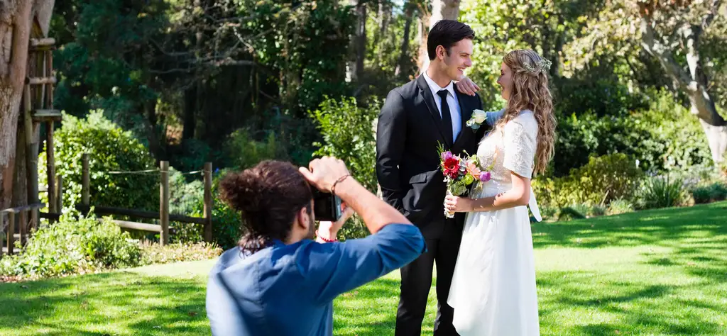 Svatební fotograf na letní zahradě fotí nevěstu s ženichem.